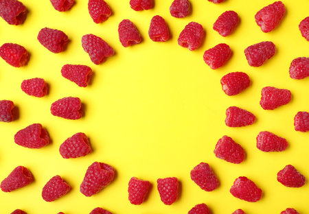 Frame made with delicious ripe raspberries on yellow background. Space for textの写真素材