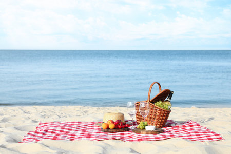 Checkered blanket with picnic basket and products on sunny beach. Space for textの写真素材