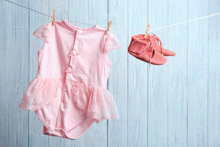 Pair of shoes and bodysuit on laundry line against wooden background. Baby accessoriesの写真素材