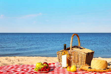 Checkered blanket with picnic basket and products on sunny beach. Space for textの写真素材