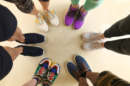 Closeup view of people in stylish training shoes standing on floor indoors, top view