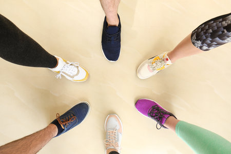 Closeup view of people in stylish training shoes standing on floor indoors, top view