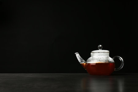Glass teapot with delicious hot beverage on table against dark background. Space for textの写真素材