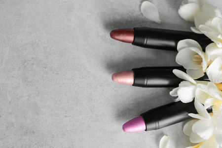 Set of bright lipsticks and spring flowers on gray background, flat lay. Space for textの写真素材