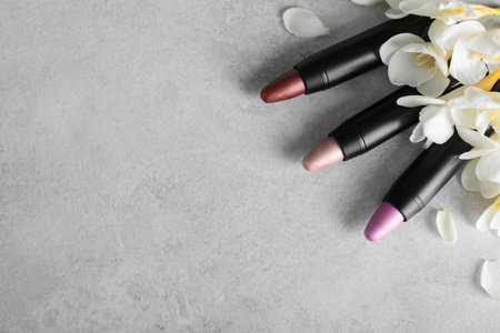 Set of bright lipsticks and spring flowers on gray background, flat lay. Space for textの写真素材