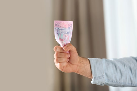 Man holding 200 Ukrainian Hryvnias banknote against blurred background, closeup with space for text....