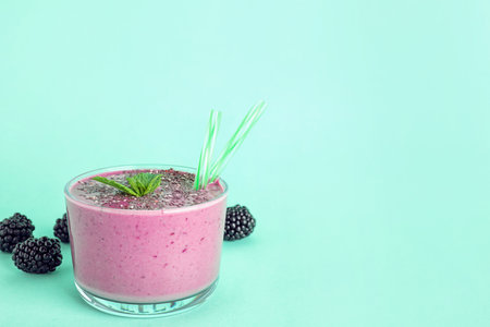 Glass of tasty blackberry smoothie with chia seeds and straws on turquoise background. Space for textの写真素材