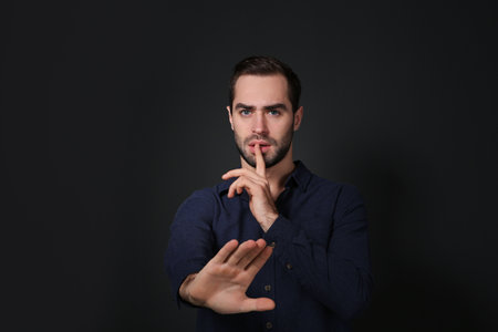 Man showing HUSH gesture in sign language on black backgroundの写真素材
