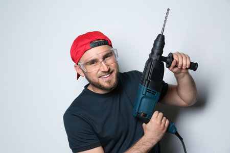 Young working man with rotary hammer on light background