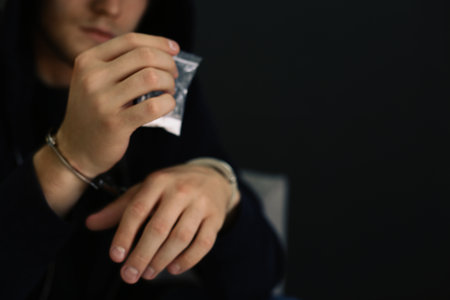 Man detained in handcuffs holding bag with drug against dark background, space for text. criminal lawの写真素材