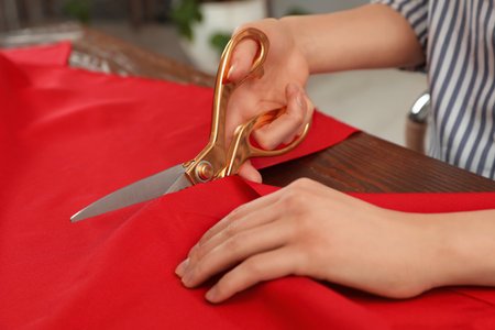 Woman cutting fabric with sharp scissors at wooden table indoors, closeupの写真素材