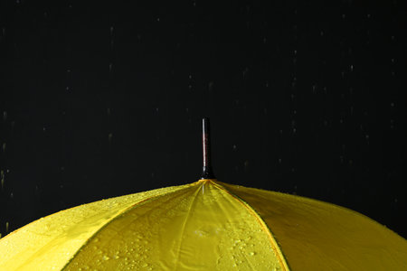 Opened yellow umbrella under rain against black background, closeup