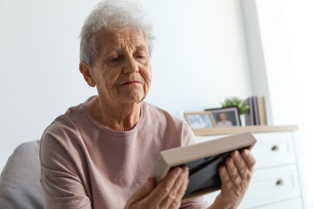 Elderly woman with framed photo at homeの写真素材
