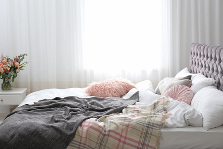 Comfortable bed with plaids and pillows in the roomの写真素材