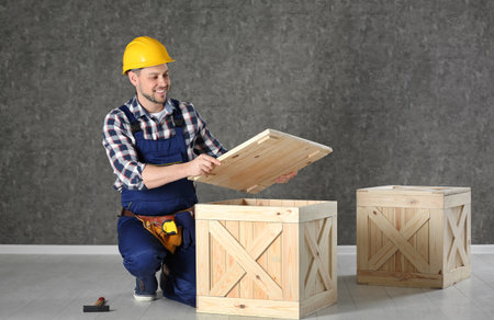Handsome man in hard hat working with wooden crate near color wallの写真素材