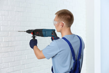 Handsome young working man using rotary hammer indoors. home repairの写真素材