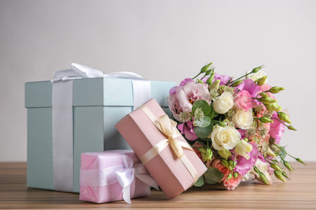Beautiful bouquet of flowers and gift boxes on wooden table against light backgroundの写真素材