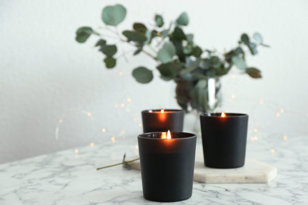 Burning candles and green branches with fairy lights on marble tableの写真素材