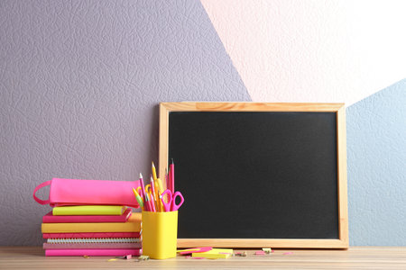 Different school stationery and small blank chalkboard on table near color wall. Space for textの写真素材