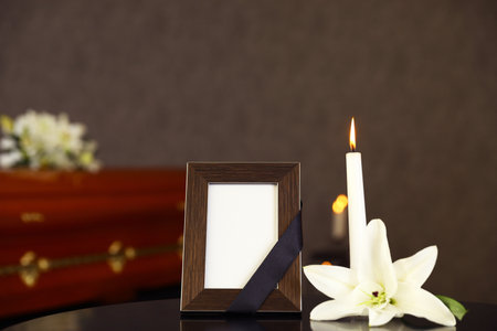 Black photo frame with burning candle and white lily on table in funeral home