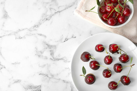 Plate of chocolate dipped cherries on white marble table, flat lay. Space for textの写真素材
