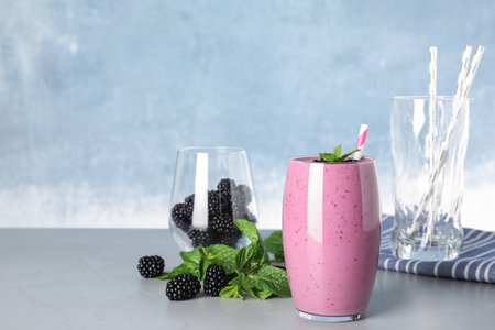 Glass of tasty blackberry smoothie and ingredients on gray table. Space for textの写真素材