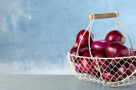 Metal basket with red onions on gray table, space for textの写真素材