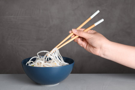 Woman eating cooked Asian noodles with chopsticks on table against gray background, closeupの写真素材