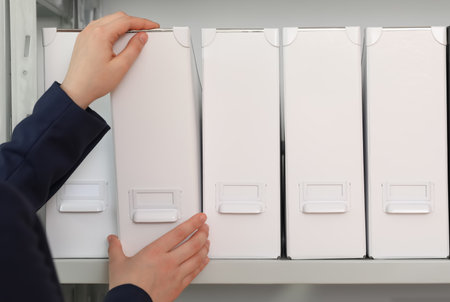 Woman taking folder with documents from shelf in archive, closeupの写真素材
