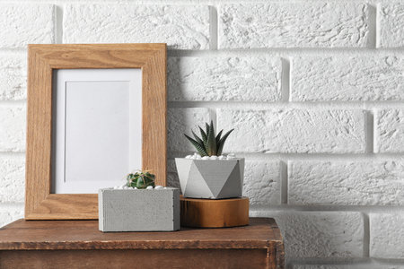 Blank frame and succulent plants on wooden cabinet near white brick wall, space for design. home...