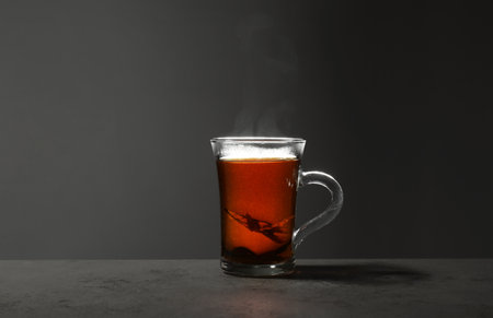 Glass cup of hot leaf tea on stone table against gray background, space for textの写真素材