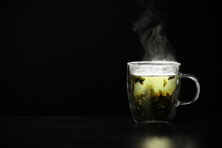 Glass cup of hot green tea on table against black background, space for textの写真素材