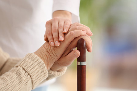 Nurse comforting elderly woman with cane against blurred background, closeup. Assisting senior generationの写真素材