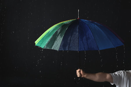 Man holding color umbrella under rain against black background, closeupの写真素材