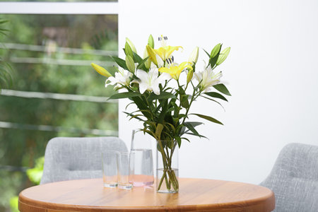 Vase with bouquet of beautiful lilies on wooden table indoorsの写真素材