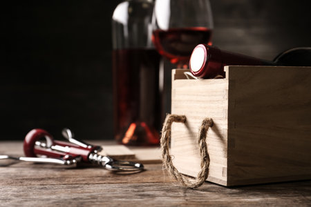 Open wooden crate with bottle of wine and corkscrew on table, space for textの写真素材