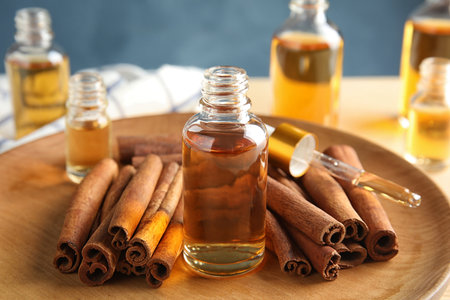 Bottles of essential oils and cinnamon sticks on wooden plate, closeupの写真素材