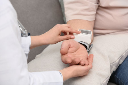 Nurse measuring blood pressure of elderly man against gray background, closeup. Assisting senior...