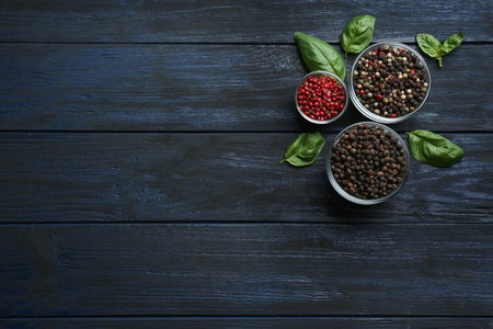Different peppercorns in bowls on dark wooden table, top view. Space for text