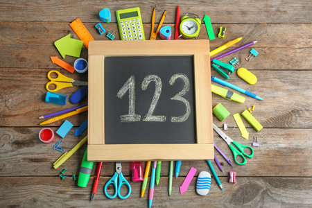Small chalkboard with numbers and different school stationery on wooden background, flat layの写真素材