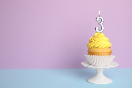 Birthday cupcake with number three candle on stand against color background, space for textの写真素材