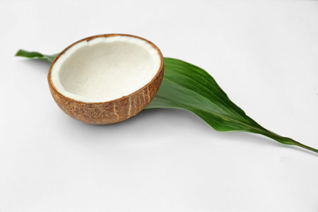 Half of fresh coconut and palm leaf on white backgroundの写真素材