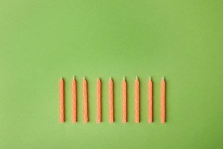Orange birthday candles on green background, top view with space for textの写真素材