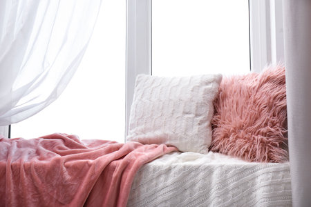 Soft pillows and plaids on window sill in room. Cozy place to relaxの写真素材