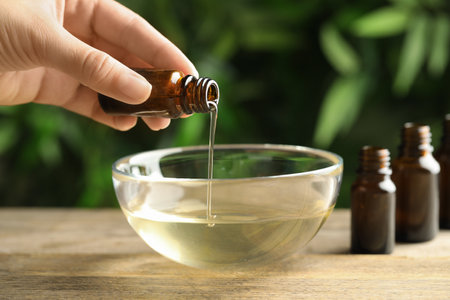 Woman pouring essential oil from glass bottle into bowl on table, closeupの写真素材