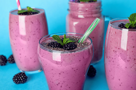 Glasses with tasty blackberry smoothie on blue background, closeupの写真素材