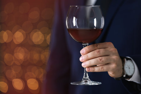 Man in formal suit with glass of wine against blurred background, closeup. Space for textの写真素材