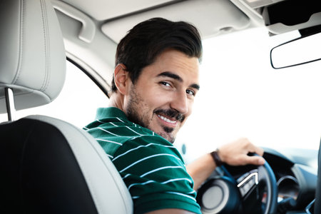 Attractive young man driving luxury car, view from backseatの写真素材