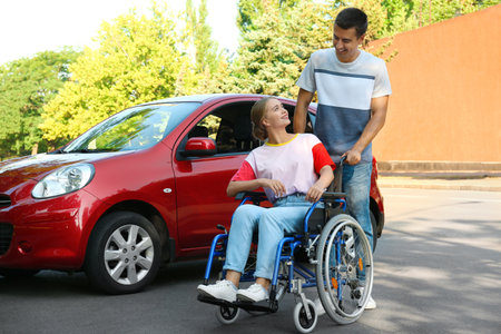 Young man with disabled woman in wheelchair near car outdoorsの写真素材
