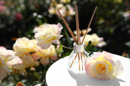 Reed air freshener with oil and fresh rose on table against blurred background. Space for text